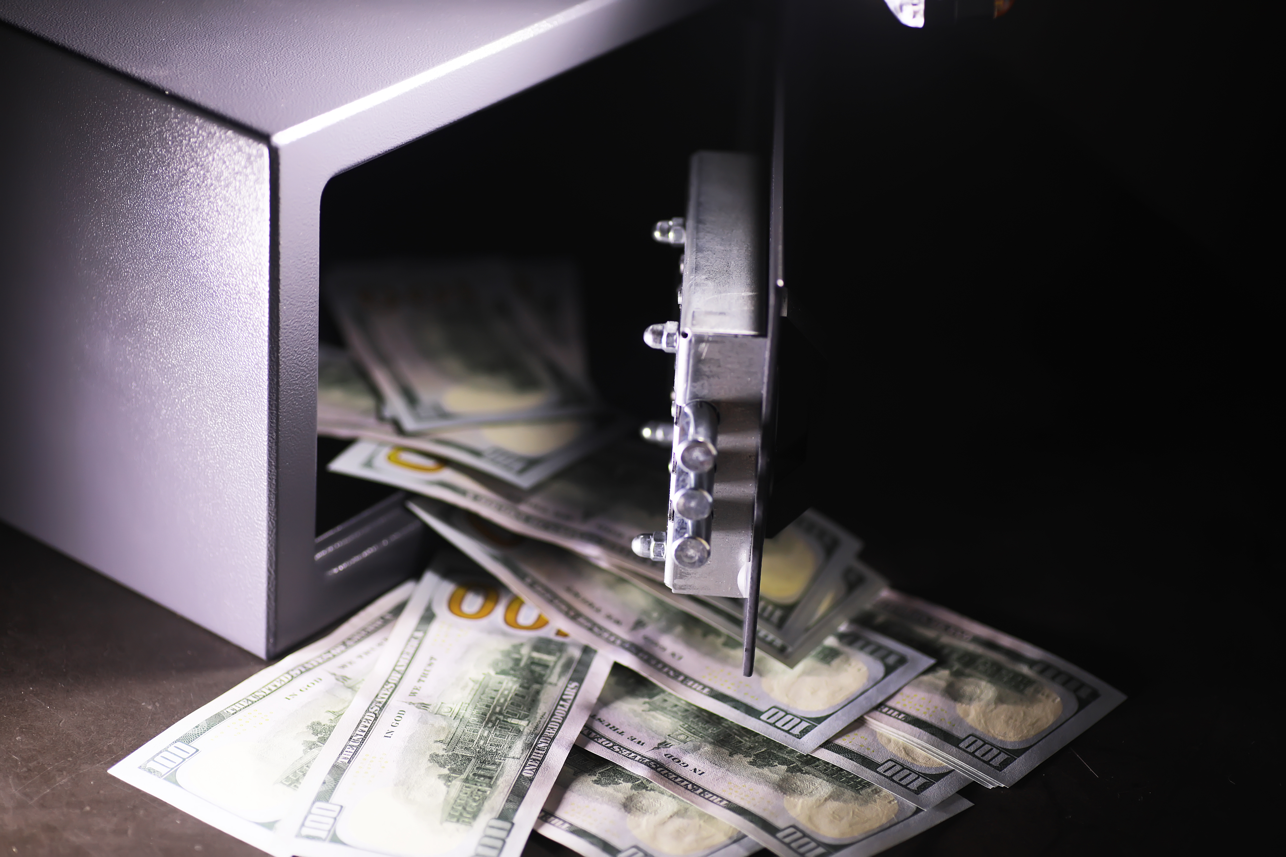 An open safe with USA one hundred dollar bills spilling out. e