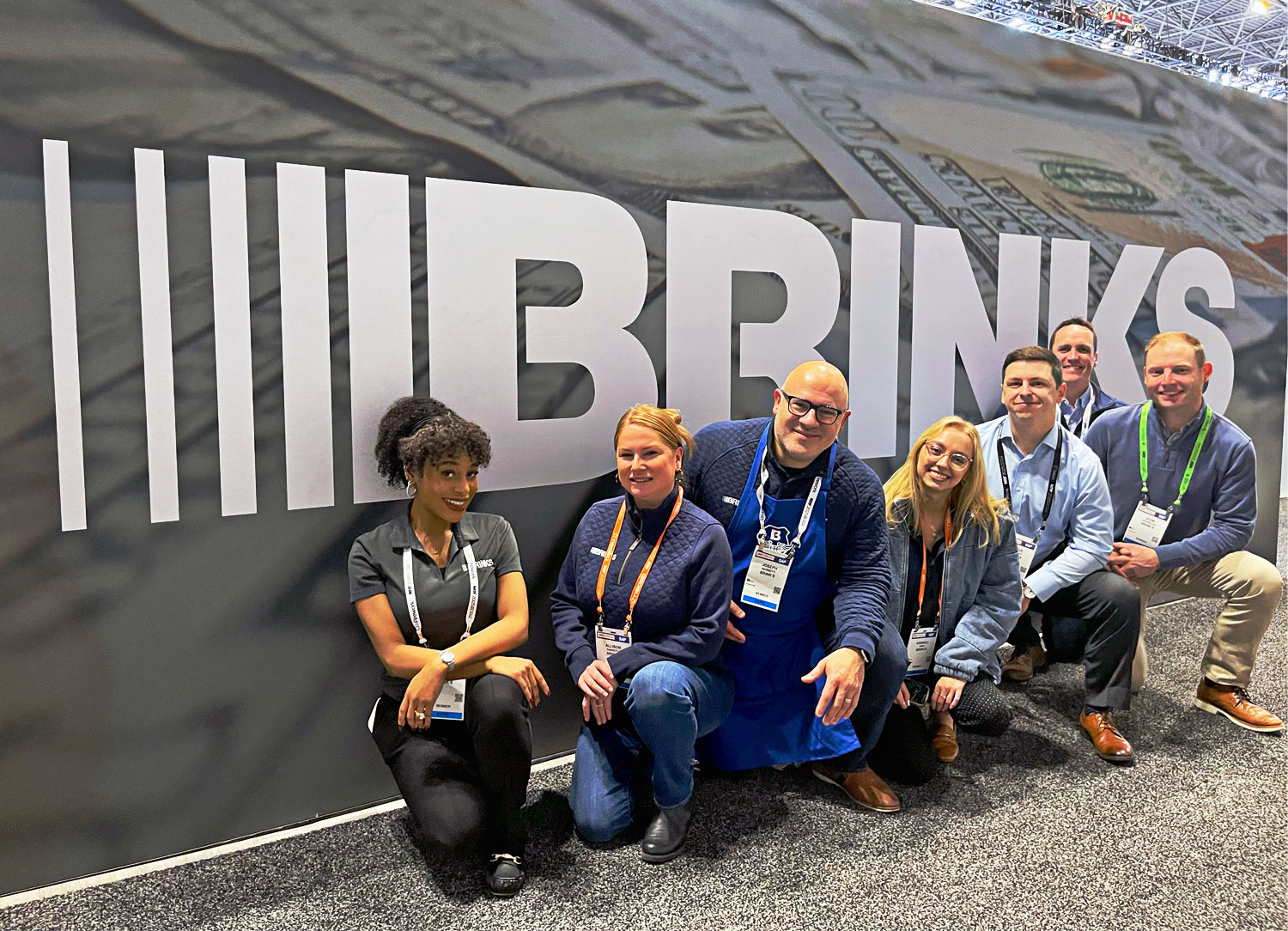 A group of Brink's team members poses in front of a large Brink's logo backdrop at the NRF 2025 event.