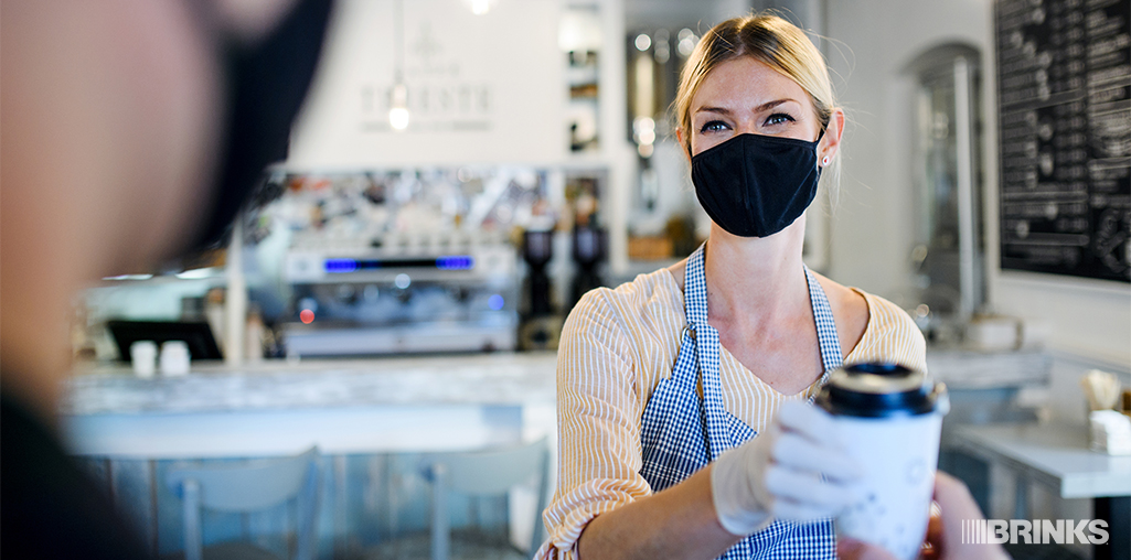A masked retail employee serves customers with social distancing measures in place.